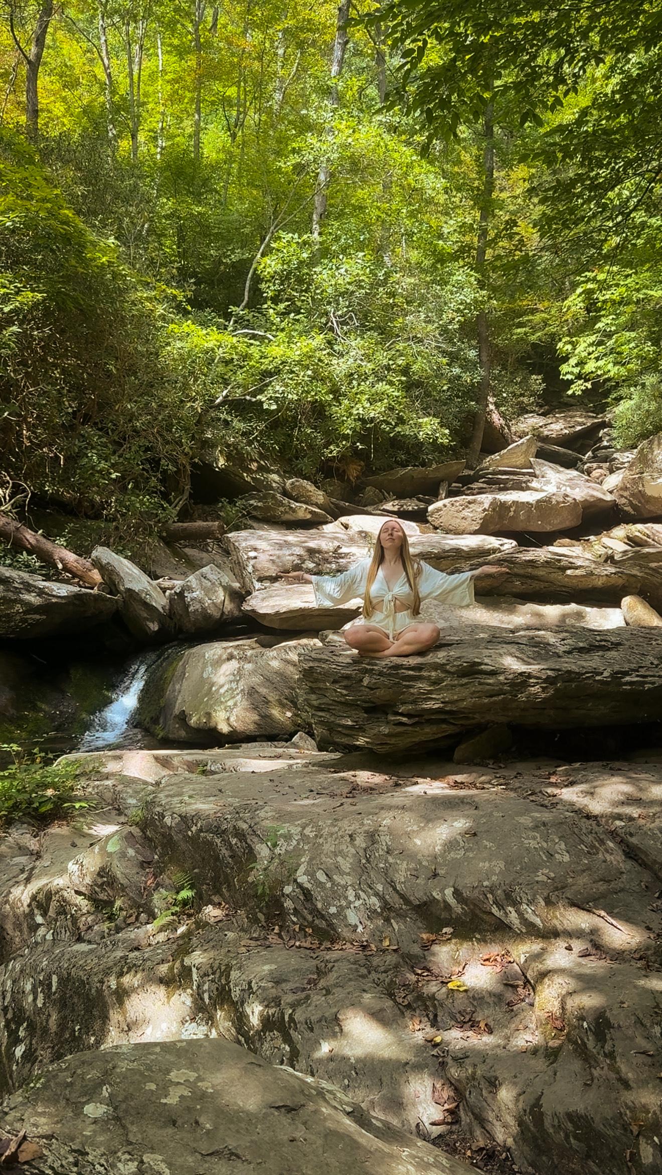 Ashley sitting in meditation on rocks beside a waterfall